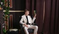 Bored teen student guy in white business suit sitting in a chair with a book by the fireplace Royalty Free Stock Photo