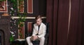 Bored teen student guy in white business suit sitting in a chair with a book by the fireplace Royalty Free Stock Photo