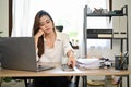 Bored and tired Asian businesswoman at her office desk, about to use her smartphone Royalty Free Stock Photo