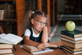 Bored and tired. Cute little girl with pigtails is in the library. Apple on the books Royalty Free Stock Photo