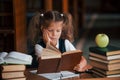 Bored and tired. Cute little girl with pigtails is in the library. Apple on the books Royalty Free Stock Photo