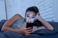 Bored and tired pretty young woman using mobile phone in bed. Royalty Free Stock Photo