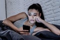 Bored and tired pretty young woman using mobile phone in bed. Royalty Free Stock Photo