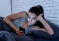 Bored and tired pretty young woman using mobile phone in bed. Royalty Free Stock Photo