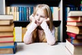 Bored and tired schoolgirl studying with a pile of books