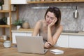 Young attractive woman sitting at the table and working on laptop in the kitchen at home Royalty Free Stock Photo