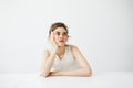 Bored tired young pretty girl with bun thinking dreaming sitting at table over white background. Royalty Free Stock Photo