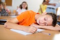 Bored tween schoolboy sleeping at desk in classroom during lesson Royalty Free Stock Photo