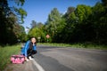 Bored of waiting to hitchhike, a teenager waits at the side of a road leading through a leafy forest on a sunny day. Royalty Free Stock Photo