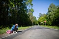 Bored of waiting to hitchhike, a teenager waits at the side of a road leading through a leafy forest on a sunny day. Royalty Free Stock Photo