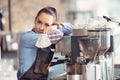 Bored waitress leans against the coffee machine with no job to do, holding face mask in her hand