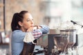 Bored waitress leans against the coffee machine with no job to do, holding face mask in her hand