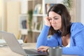 Bored woman checking laptop on a desk at home