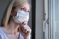 Bored woman in surgical face mask staying at home and looking through the window, covid-19 quarantine and self isolation