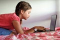 Bored young girl age 10 using a laptop in bedroom while forced to stay at home because government policies efforts to prevent Royalty Free Stock Photo