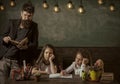 Boring lesson concept. Teacher and girls pupils in classroom, chalkboard on background. Man with beard teaches