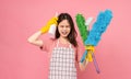 Boring young Asian woman wearing apron with yellow rubber gloves and holding bucket of cleaning supplies on pink background Royalty Free Stock Photo