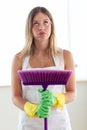 Boring young woman holding broom while cleaning at home.