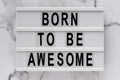 `Born to be awesome` words on a lightbox on a marble background, top view. Overhead, from above, flat lay