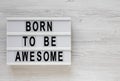 `Born to be awesome` words on a lightbox on a white wooden background, top view. Overhead, from above, flat lay. Copy space