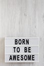 `Born to be awesome` words on a lightbox on a white wooden background, top view. Overhead, from above, flat lay. Copy space