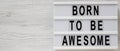 `Born to be awesome` words on a lightbox on a white wooden background, top view. Overhead, from above, flat lay. Space for text