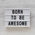 `Born to be awesome` words on a modern board on a white wooden background, top view. Overhead, from above, flat lay