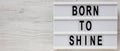 `Born to shine` words on a lightbox on a white wooden background, top view. Overhead, from above, flat lay. Space for text