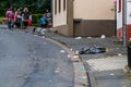 Trash recklessly dumped on the street and sidewalk after a carnival parade. People in costumes are celebrating.