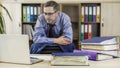 Boss businessman at his desk in the office with a bunch of folders. Leans against the back of the chair and looks at the laptop.