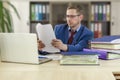 Boss businessman at his desk in the office examines documents. Financial check. Preparation of a report by an office worker