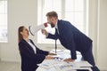 Boss businessman shouting in magaphone at businesswoman employee secretary at desk in office Royalty Free Stock Photo