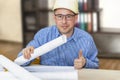 The boss in the construction helmet at the table with the project documentation shows his thumb. Successful completion of the