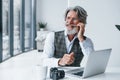 Boss in formal clothes works in office. Senior stylish modern man with grey hair and beard indoors