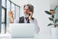 Boss in formal clothes works in office. Senior stylish modern man with grey hair and beard indoors