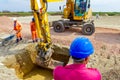 Boss oversees, controlling excavator until is digging on building site