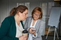 Boss using her smartphone while interested woman peeking into it