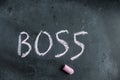 Boss. A word written in pink chalk on a black chalkboard. Handwritten text. A piece of colored chalk hangs next to it