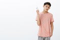 Bossy serious-looking cool young teenage asian guy in striped t-shirt taking away smartphone as being distracted. Guy