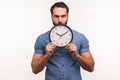 Bossy serious man with beard holding in hands big wall clock looking at camera with displeased, time to act, countdown