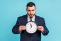 Bossy serious man with beard wearing official style suit holding in hands big wall clock looking at