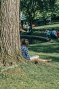 Boston, US - June 3: Young female sketching leaning on a tree in a park by the lake in Public Garden in Boston