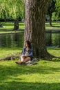 Boston, US - June 3,2019 : Young female sketching leaning on a tree in a park by the lake in Public Garden in Boston