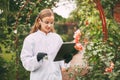 A botanist woman holding a tablet and a magnifying glass examines a plant sample during a quality check.