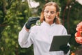 A botanist woman holding a tablet and a magnifying glass examines a plant sample during a quality check.