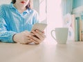 both hand hold smart phone and put white hot coffee cup for drink in morning time on table with soft focus background of beauty Royalty Free Stock Photo