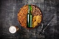 A bottle of beer on a plate with salted ookies pretzels, pistachio nuts and chips on a black scratched chalk board