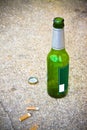 Bottle of beer resting on the ground with three cigarette's Royalty Free Stock Photo