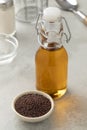 Bottle with brown mustard oil and bowl with black mustard seeds in front