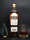 A bottle of Bushmills whiskey, a glass of whiskey and a small new Christmas tree on a black background